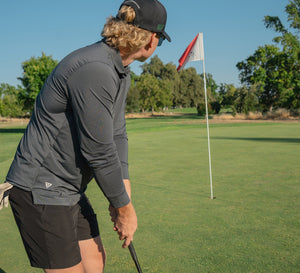 Influencer wearing MAELREG black stripe long-sleeve polo in side view preparing to swing on golf course