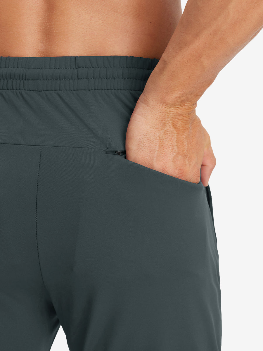 Back view of model with hand in pocket wearing lightweight traning track pants in dark grey.